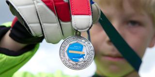 Ein Junge hält eine gewonne Medaille in die Kamera. (Foto: picture alliance / augenklick/firo Sportphoto | firo Sportphoto)