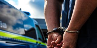 Eine Person wird durch die Polizei festgenommen, es wurden die Handschellen angelegt. Im Hintergrund sieht man den Streifenwagen der Polizei stehen. (Foto: picture alliance / Fotostand | Fotostand / K. Schmitt)