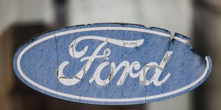 Ein abgeblättertes Logo von Ford hängt an einer Scheibe vor dem Werksgelände. (Foto: picture alliance/dpa | Oliver Berg)