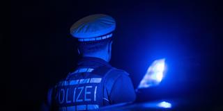 Ein Polizist steht neben einem Polizeifahrzeug mit Blaulicht. (Foto: picture alliance/dpa | Marijan Murat)