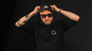 Ein Mann steht mit Sonnenbrille und schwarzer Kappe vor einem schwarzen Hintergrund. Er trägt einen schwarzen Hoodie und hat die Kapuze aufgesetzt. (Foto: Pressefoto)