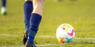 Symbolbild: Ein Fußball liegt vor Spieler-Füßen auf einem Rasenplatz (Foto: IMAGO / Hanno Bode)