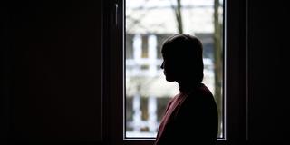 Eine Frau sitzt im dunklen Zimmer und schaut aus dem Fenster. (Foto: IMAGO / Funke Foto Services)