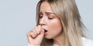 Eine junge Frau hustet sich in die Hand (Foto: IMAGO / Zoonar)