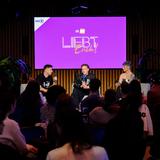 Blick auf eine Bühne, auf der drei personen sitzen. Im Hintergrund ist ein lila "Liebt Euch" Poster zu sehen. (Foto: Liebt Euch Podcast)