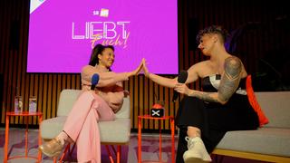 Zwie Frauen sitzen nebeneinander und schauen sich an. Dabei berühen sich ihre Hände. (Foto: Liebt Euch Podcast)