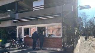 Vor dem Ausgabefenster des Parkdeck-Dönerladens stehen zwei Menschen und warten auf ihr Essen. Die Sonne scheint. (Foto: UNSERDING)